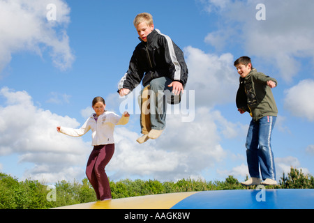 three kids jumping on a big rubber trampoline Stock Photo