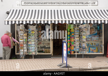Man and woman tourists eating ice creams looking at postcard racks outside shop Llangollen north east wales UK Stock Photo