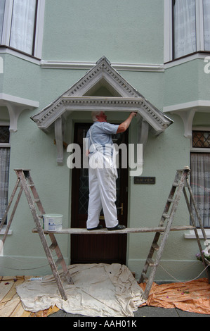 self employed painter standing on platform between two step ladders painting the porch of a house grey Stock Photo