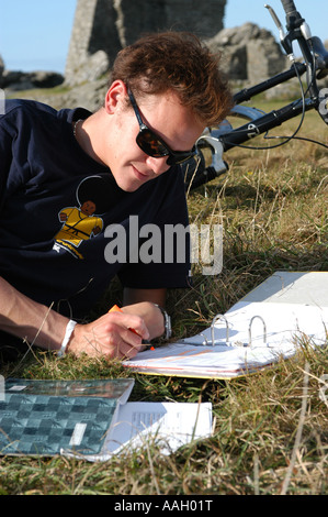 Young male student Aberystwyth university reading outdoors in the sunshine in the castle with his bicycle behind him, Wales UK Stock Photo