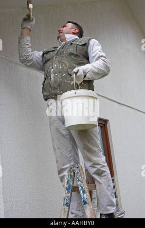 Young man standing on ladder painting a wall with a paint brush Stock Photo