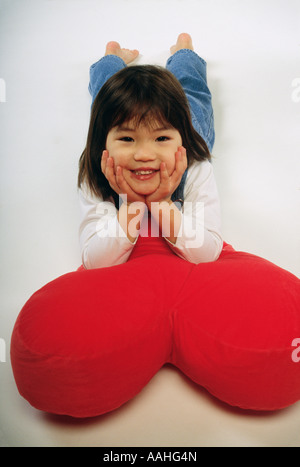 Girl 4 5 lying on heart shaped cushion smiling portrait Stock Photo