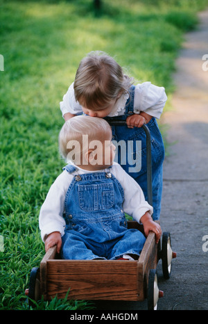 Young boy pushing younger brother in wooden wagon Stock Photo