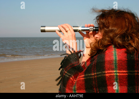 Woman looking out to sea through a telescope. Stock Photo