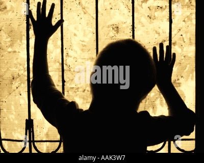 Little boy silhouetted behind the bars of a window Stock Photo