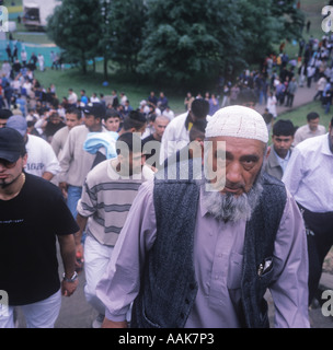 A muslim man leads visitors walking up a hill towards the Bradford Mela, Peel Park, Bradford, UK, June 2004. Stock Photo