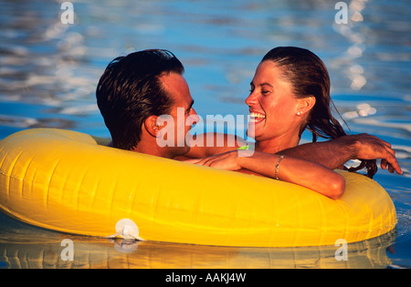 1980s HAPPY YOUNG COUPLE FLOATING IN PLASTIC INNER TUBE IN THE POOL Stock Photo