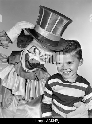 1950s SMILING CLOWN WITH TOP HAT ARM AROUND GRINNING BOY IN STRIPED SHIRT Stock Photo