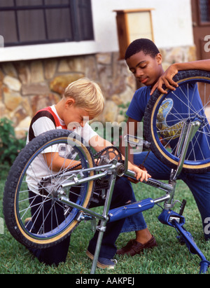 1980s AFRICAN AMERICAN AND CAUCASIAN BOYS FRIENDS WORKING TOGETHER FIXING A BICYCLE Stock Photo