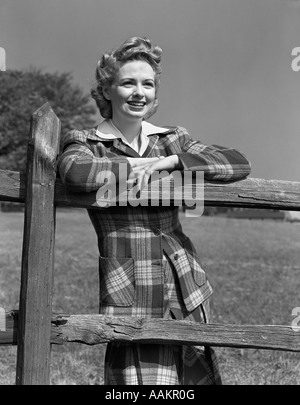 1940s BLOND WOMAN SMILING LEANING ARMS ON WOODEN FENCE WEARING PLAID TARTAN SUIT Stock Photo