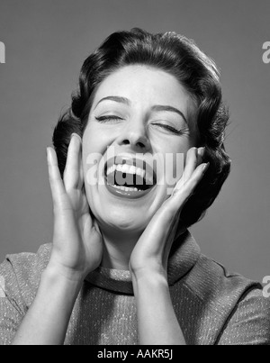1950s 1960s HAPPY BRUNETTE WOMAN SMILING LAUGHING YELLING HANDS TO CHEEKS EYES CLOSED Stock Photo