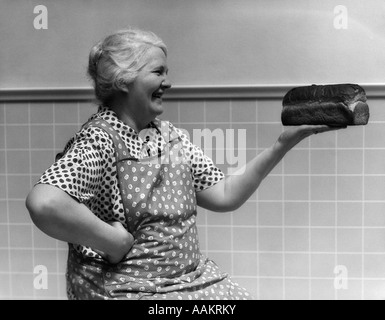 1930s 1940s GRANDMOTHER IN APRON ADMIRING LOAF OF FRESHLY BAKED BREAD Stock Photo
