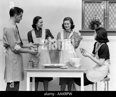 1930s 1940s WOMEN 1 MAN APRONS IN KITCHEN PULLING TAFFY Stock Photo
