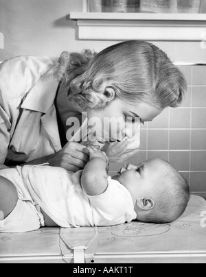 1950s MOTHER WOMAN BENDING OVER BABY LYING ON LAYETTE HOLDING HANDS TALKING Stock Photo