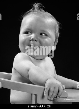 1950s 1940s BABY IN HIGH CHAIR HEAD TURNED TO ONE SIDE WITH TONGUE STICKING OUT FUNNY FACIAL EXPRESSION Stock Photo