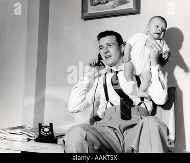 1950s FATHER HOLDING BABY WHILE ON THE PHONE Stock Photo