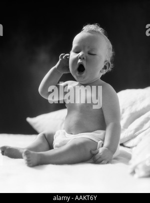 1930s BABY SITTING UP IN BED FACING CAMERA YAWNING TIRED SLEEPY Stock Photo