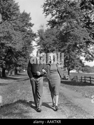 1930s 1940s YOUNG TEENAGE COUPLE BOY GIRL STROLLING DOWN AUTUMN COUNTRY LANE ARM IN ARM Stock Photo