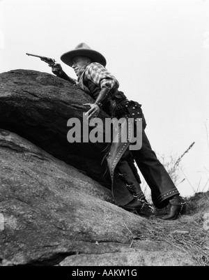 1920s COWBOY AMONG ROCKS AIMING REVOLVER Stock Photo