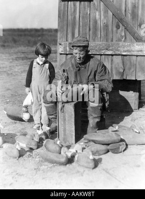 1920s 1930s SMALL BOY WATCHING OLDER MAN ASSEMBLE DUCK DECOYS Stock Photo