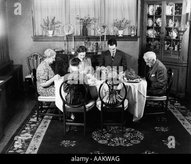 1940s EXTENDED FAMILY SITTING AROUND DINING ROOM TABLE SAYING GRACE BEFORE THANKSGIVING DINNER Stock Photo