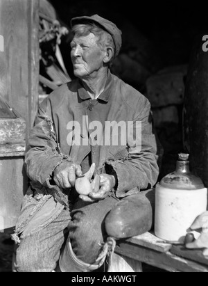 1920s 1930s ELDERLY MAN WEATHERED FACE SITTING BESIDE JUG CARVING WOODEN DUCK DECOY HEAD BARNEGAT BAY NEW JERSEY USA Stock Photo