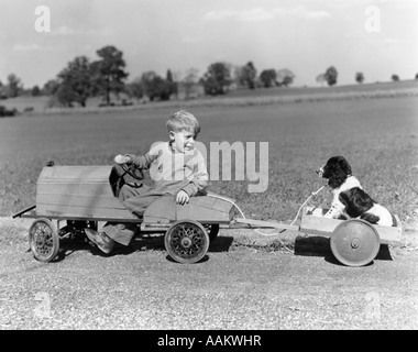 1930s 1940s BOY IN WOODEN TOY CAR PULLING DOG BEHIND IN WAGON Stock Photo
