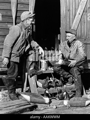 1930s 1940s TWO SENIOR MEN WEARING HUNTING CLOTHES REPAIRING WOODEN CANADA GOOSE DECOYS BARNEGAT BAY NEW JERSEY USA Stock Photo