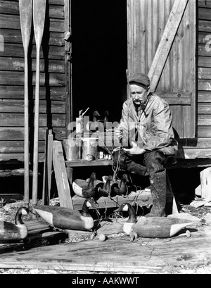 1930s 1940s SENIOR MAN SITTING ON STAIRS TO HUNTING SHACK PAINTING WOOD CANADA GEESE DECOYS BARNEGAT BAY NEW JERSEY USA Stock Photo