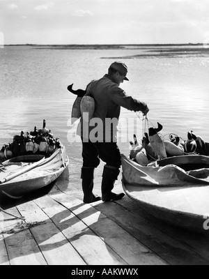 1930s 1940s HUNTER PUTTING CANADA GOOSE DECOYS INTO SNEAK-BOX WOODEN HUNTING BOAT BARNEGAT BAY NEW JERSEY USA Stock Photo