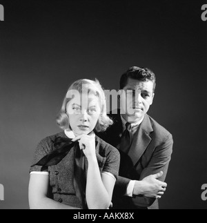 1950s COUPLE MAN BLOND WOMAN WITH SERIOUS PUZZLED EXPRESSIONS PORTRAIT LOOKING AT CAMERA Stock Photo