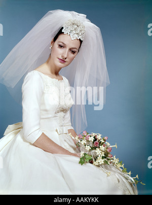 1960s FORMAL PORTRAIT OF BRIDE SITTING HOLDING FLOWER BOUQUET Stock Photo