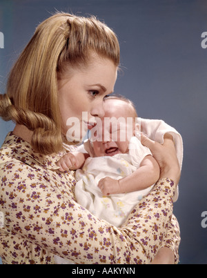 1960s CLOSE-UP OF MOTHER HOLDING CRYING BABY INFANT WOMAN FUSSING PROFILE CUDDLING Stock Photo