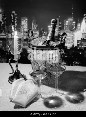 CHAMPAGNE BOTTLE IN ICE BUCKET WITH GLASSES CANDLE & NAPKINS ON TABLE & NEW YORK CITY NIGHT SKYLINE IN BACKGROUND Stock Photo