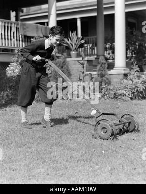 1930s 1920s BOY PUSHING LAWN MOWER WEARING KNICKERS CUTTING THE GRASS Stock Photo
