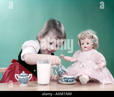 1950s LITTLE GIRL TODDLER AND BABY DOLL HAVING TEA PARTY BLUE WILLOW CUP SAUCER AND BIG GLASS OF MILK Stock Photo