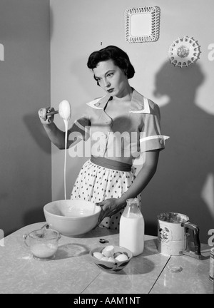 1960s HOUSEWIFE MIXING STICKY BATTER IN KITCHEN Stock Photo