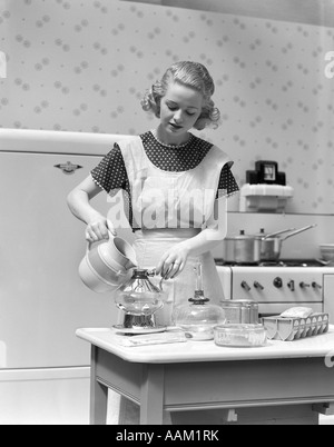 1930s WOMAN IN KITCHEN WEARING APRON MAKING BREAKFAST POURING WATER INTO COFFEE POT Stock Photo