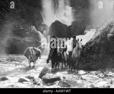 1930s TWO MEN AND WOMAN RIDING HORSEBACK WITH FOURTH HORSE CARRYING SUPPLIES IN STREAM Stock Photo