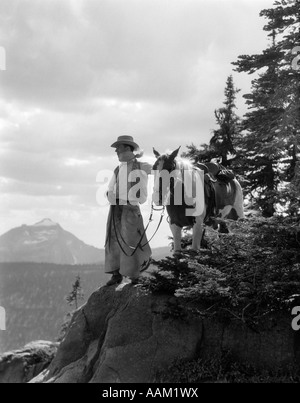 1940s MAN COWBOY IN CHAPS VEST HAT AND KERCHIEF WITH PALOMINO HORSE ON PEAK OVERLOOKING GLACIER PARK MONTANA USA Stock Photo