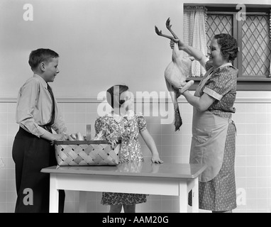 1940s HOUSEWIFE SHOWING RAW FRESH PLUCKED TURKEY TO SON AND DAUGHTER IN KITCHEN Stock Photo