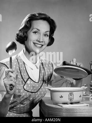 1960s WOMAN HOUSEWIFE ABOUT TO STIR POT WITH SPOON SMILING COOKING Stock Photo