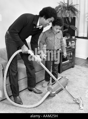1970s 1980s AFRICAN AMERICAN MAN FATHER AND SON BOY VACUUMING CARPET VACUUM Stock Photo