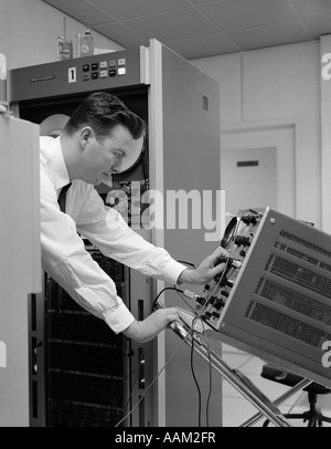 1960s SIDE VIEW OF MAN IN SHIRT & TIE USING OSCILLOSCOPE TO CHECK ELECTRONIC COMPONENTS Stock Photo