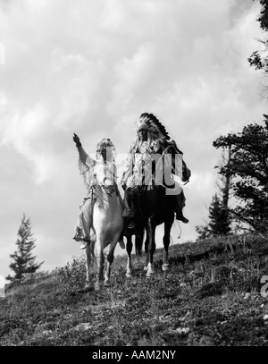 1930s PAIR OF SIOUX INDIANS IN HEADDRESSES ON HORSEBACK POINTING OUT TRAIL Stock Photo