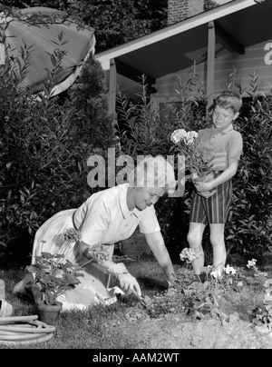 1960s BOY HELPING GRANDMOTHER PLANT FLOWERS IN GARDEN Stock Photo