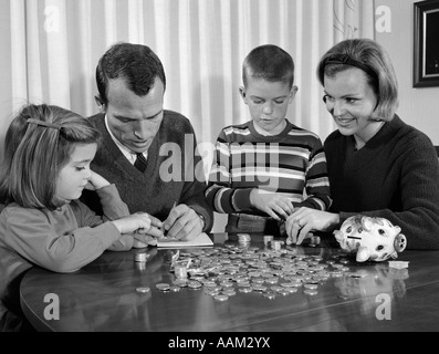 1960s PARENTS SEATED AT DINING ROOM TABLE WITH DAUGHTER & SON COUNTING CHANGE FROM PIGGY BANK Stock Photo