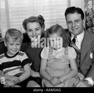 1940s 1950s PORTRAIT OF SMILING FAMILY MAN WOMAN BOY GIRL SITTING ON SOFA LOOKING AT CAMERA Stock Photo