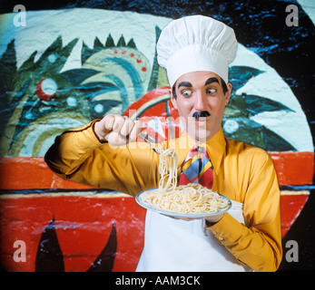 WACKY FUNNY CHARACTER MAN IN CHEF HAT APRON FAKE MOUSTACHE BROW LIFTING FORK FULL OF SPAGHETTI EXPRESSION ITALIAN Stock Photo