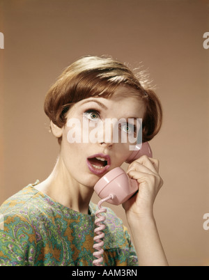 1960s WOMAN SURPRISED EXPRESSION TALKING ON PINK TELEPHONE Stock Photo